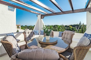 A rooftop terrace with wicker furniture, a glass table, and a potted plant. - AB26 - Lovely holiday home in Aldea Blanca (Marbella)