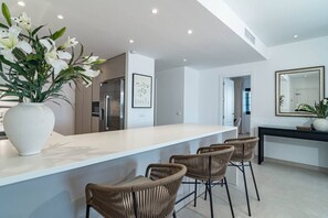 A modern kitchen with a white countertop, wicker bar stools, and a large white vase with flowers. - AB26 - Lovely holiday home in Aldea Blanca (Marbella)