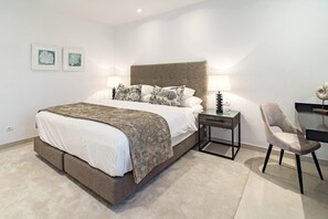 Quarto moderno com uma cama grande, mesas de cabeceira, uma cadeira e uma obra de arte na parede.