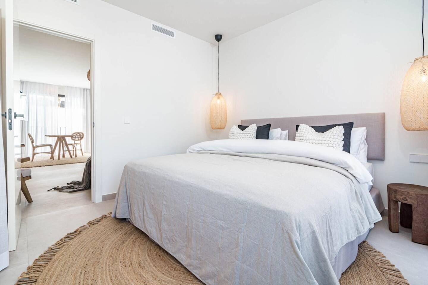 Quarto com cama, luminária pendente e vista para outro cômodo.