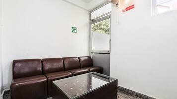 A waiting area with a brown leather couch and a glass-top table, a 'No Smoking' sign, a 'G' restroom sign, and a window with a view of trees.