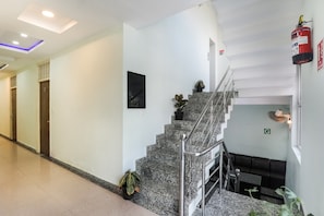 Vestíbulo de hotel con una escalera, extintor, mostrador de recepción y una planta.