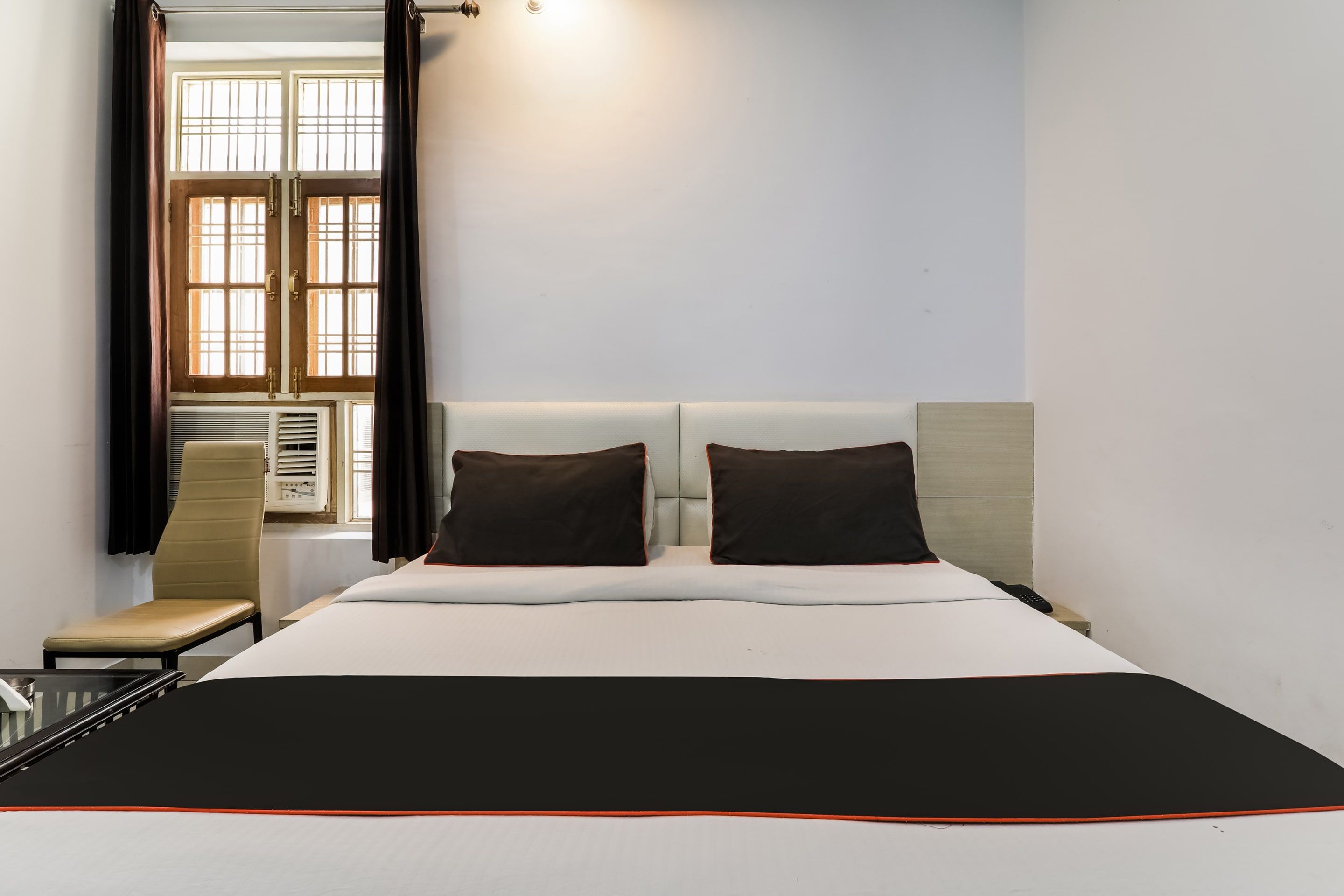 Habitación de hotel con cama, dos almohadas, una silla, ventana con cortinas y un calentador de pared.