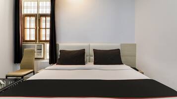 Habitación de hotel con cama, dos almohadas, una silla, ventana con cortinas y un calentador de pared.