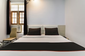Habitación de hotel con cama, dos almohadas, una silla, ventana con cortinas y un calentador de pared.