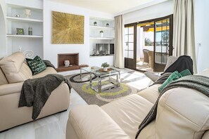 A modern living room with a beige sofa, a glass coffee table, and a fireplace. There are shelves with decorative items and a large abstract painting on the wall. - AB4 - Lovely holiday home walking distance, beach (Marbella)
