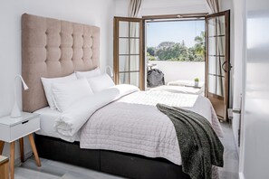 Quarto com cama grande, mesa de cabeceira e vista através de porta aberta.
