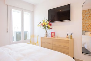 Une chambre d’hôtel avec un grand lit, un téléviseur fixé au mur, une commode en bois et une fenêtre donnant sur des immeubles.