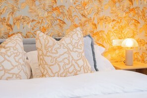 A bed with patterned pillows, a nightstand with a lamp, and a wall with a tropical leaf pattern. - AC152 - Top Renovated Modern 1 Bed with Pool (Marbella)