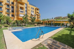 A swimming pool with a lifebuoy, surrounded by a well-maintained lawn and a multi-story building with balconies. - Penthouse Walk to Beach & Town - ADB352 (Marbella)