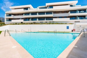 Ein modernes Gebäude mit Schwimmbad, mehreren Balkonen und blauem Himmel.