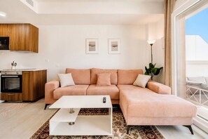 A modern living room with a sofa, coffee table, and a kitchen area with wooden cabinets and a stove. - AH2B - Modern apartment near Estepona town (Estepona)