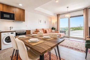 Eine moderne Küche mit Mikrowelle, Backofen und Waschmaschine. Ein Essbereich mit Tisch für vier Personen, einer Couch und einem großen Fenster mit Blick.