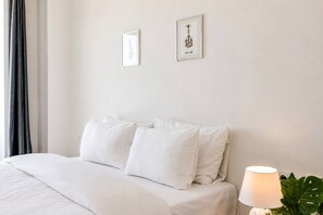 Een hotelkamer met een bed, kussens, een bedlampje en twee ingelijste foto’s aan de muur.
