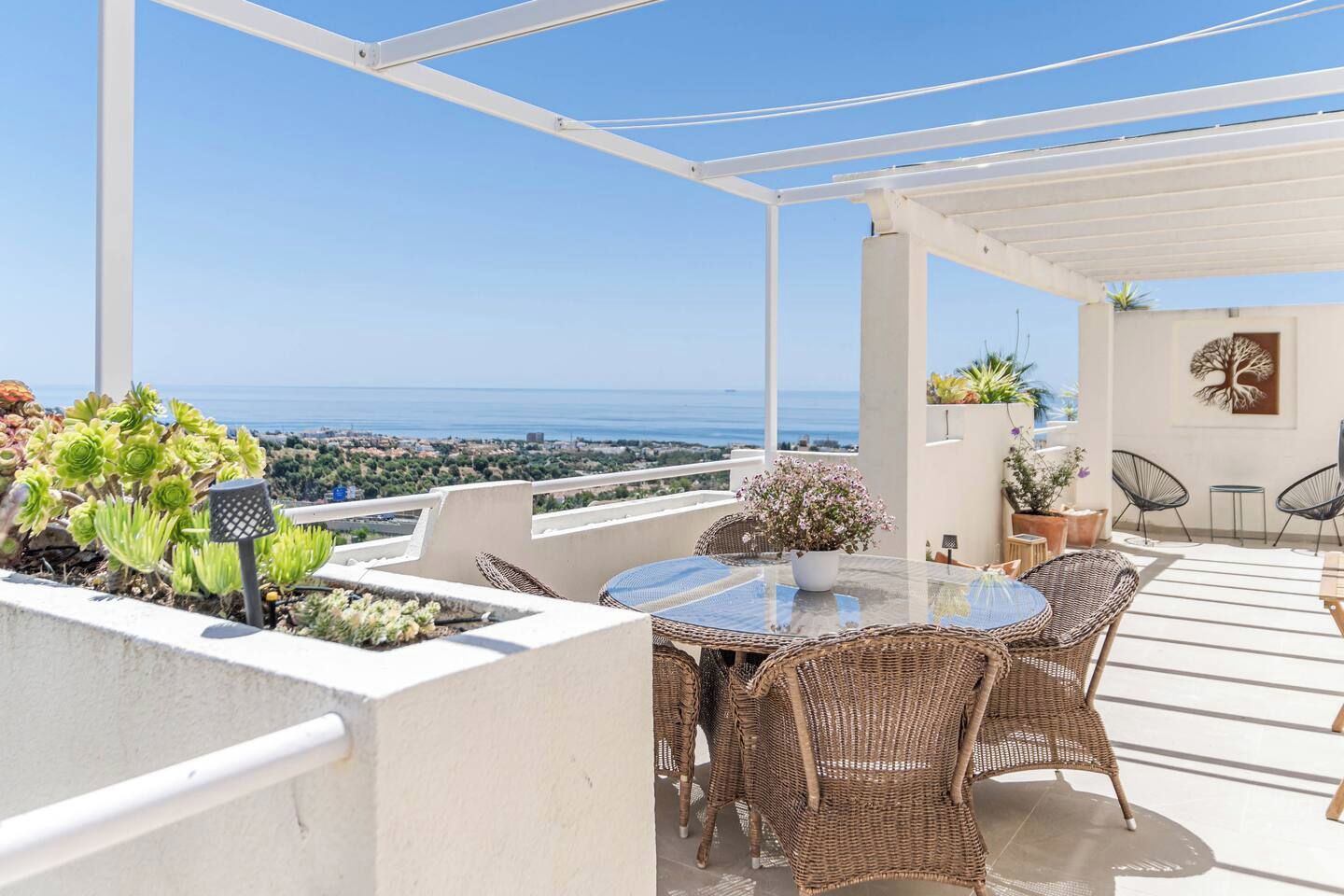 A terrace with a table and chairs, potted plants, and a view of the sea.