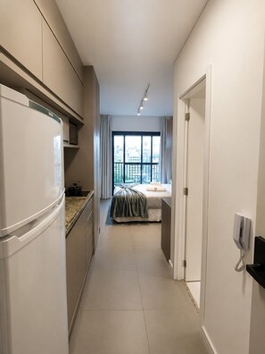 A narrow hallway leading to a bedroom with a large window, a bed, and a kitchen area with a refrigerator. - SETIN 1508 (São Paulo)