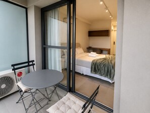 A hotel room with a bed, a small table with a chair, a window with curtains, and a wall-mounted shelf. - SETIN 1508 (São Paulo)