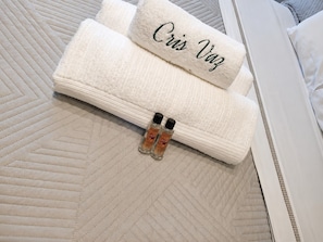 A neatly folded white towel with 'Cris Vaz' embroidered on it, placed on a textured bedspread. - SETIN 1508 (São Paulo)