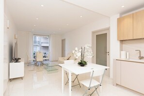A modern kitchen with white cabinetry, a white dining table, and a glass dining table. - Croisette : chic 2 chambres/ 2 salles de bains (Cannes)