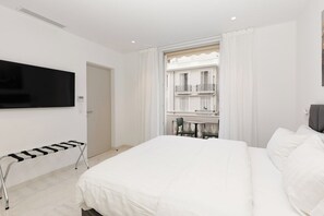 A hotel room with a bed, a TV, a window with a view of a building, and a chair. - Croisette : chic 2 chambres/ 2 salles de bains (Cannes)