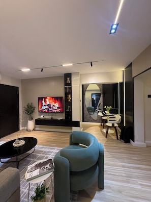 Ein modernes Wohnzimmer mit Flachbildfernseher, einer Couch, einem Couchtisch und einem Essbereich mit Tisch und Stühlen.