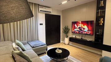 Een moderne woonkamer met een bank, een salontafel, een televisie waarop een haard te zien is, en een grote lamp.