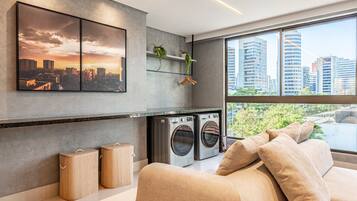 Una sala moderna con un ventanal grande, un sofá, una lavadora y vistas a un paisaje urbano.