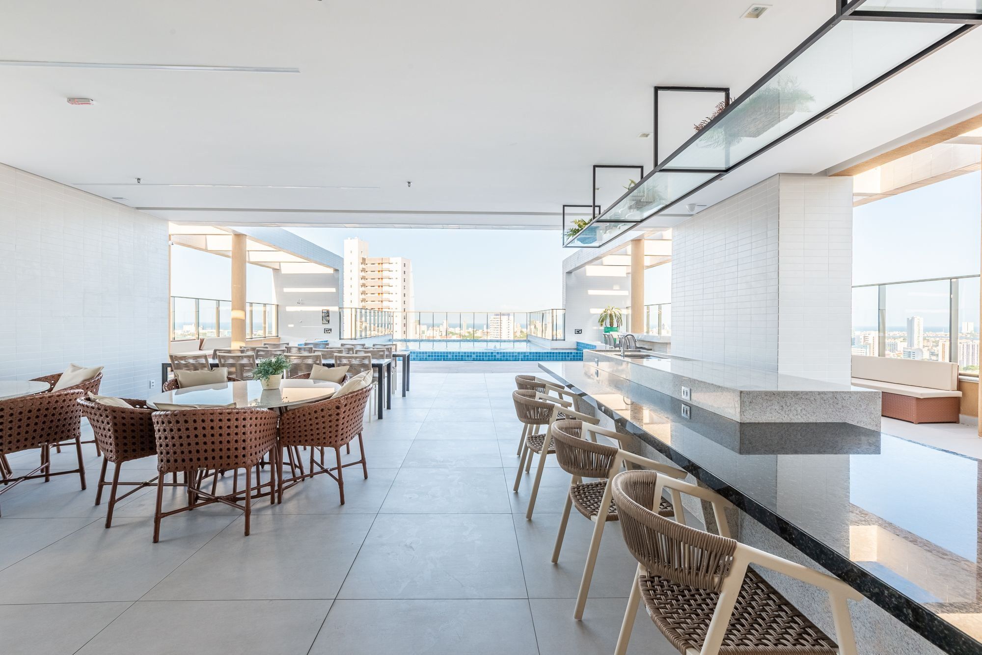 Un bar espacioso en la azotea con vista a una piscina, muebles modernos y un paisaje urbano de fondo.