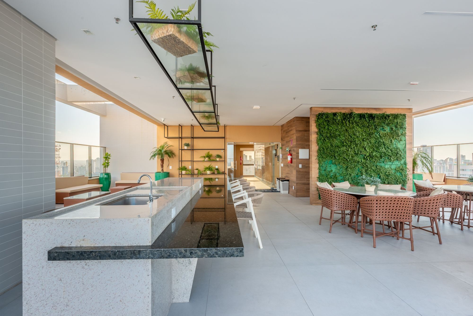 A modern kitchen with a central island, a dining area with round tables, and a green vertical garden wall.