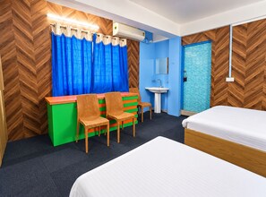 A hotel room with a bed, a desk with chairs, a sink, and a shower area. - Hotel Rangamati (Agartala)
