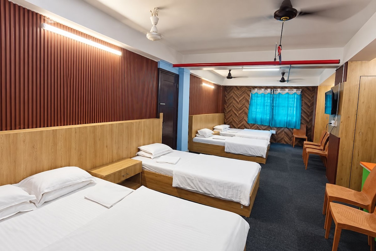 A hotel room with four single beds, a wooden headboard, a TV, and a ceiling fan.