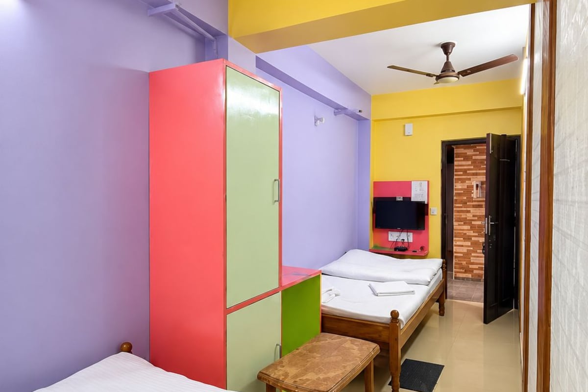 A dormitory room with two single beds, a wardrobe, a bench, and a television.