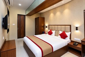 Een hotelkamer met een groot bed, een houten hoofdbord, nachtkastjes, een kledingkast en een aan de muur bevestigde televisie.