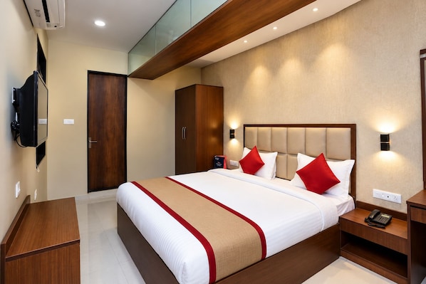 A hotel room with a large bed, wooden headboard, bedside tables, a wardrobe, and a television mounted on the wall. - Hotel Rangamati (Agartala)