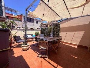 Eine Terrasse im Freien mit Tisch und Stühlen, umgeben von Topfpflanzen und einer großen Markise.