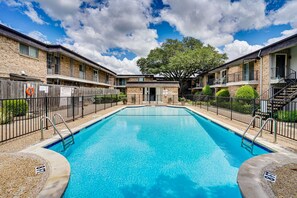 A swimming pool with a clear blue water surface, surrounded by a brick building with multiple balconies and a tree in the background. - Lovely 1-bedroom condo with AC, Wifi, Pool, Washer Dryer in vibrant Dallas (Dallas)