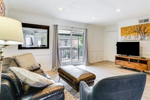 A living room with a sofa, ottoman, and a television on a wooden cabinet. - Lovely 1-bedroom condo with AC, Wifi, Pool, Washer Dryer in vibrant Dallas (Dallas)