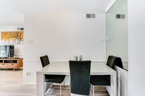 A dining area with a white table and four chairs, a television on a wooden cabinet, and a painting on the wall. - Lovely 1-bedroom condo with AC, Wifi, Pool, Washer Dryer in vibrant Dallas (Dallas)