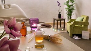 A spa setting with a massage table, a bottle of oil, a candle, and a green chair. - Résidence CGH les Chalets de Flambeau (Val-Cenis)