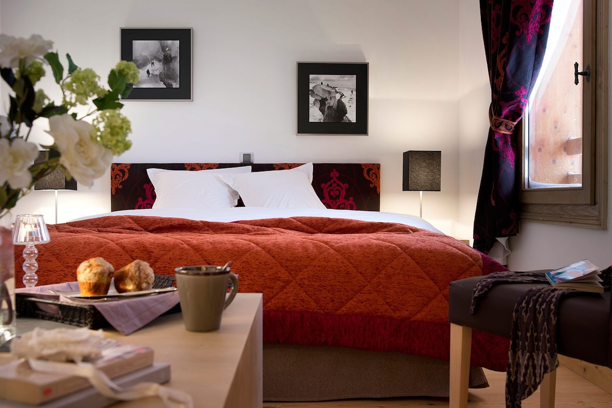 A hotel room with a bed, bedside tables, a desk with a chair, and two framed pictures on the wall.