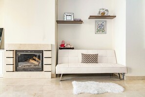 A living room with a fireplace, a white sofa, a fluffy rug, and decorative shelves. - BVQ - Stunning Sea & Golf View Terrace (Marbella)