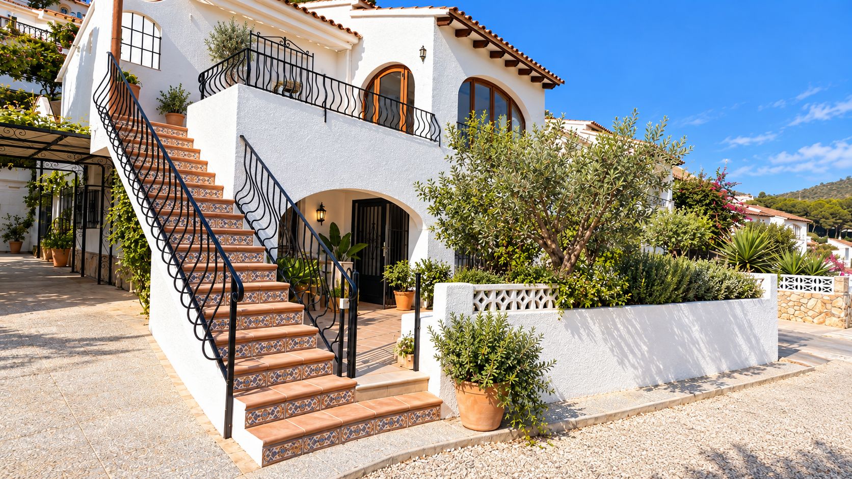 A two-story building with a staircase leading to an entrance, surrounded by potted plants and a white wall.