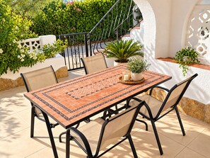 Eine Terrasse im Freien mit einem gefliesten Tisch, Stühlen und Topfpflanzen.