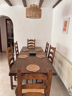 Ein Esszimmer mit Holztisch, sechs Stühlen, gewebten Tischsets und einer Hängeleuchte.