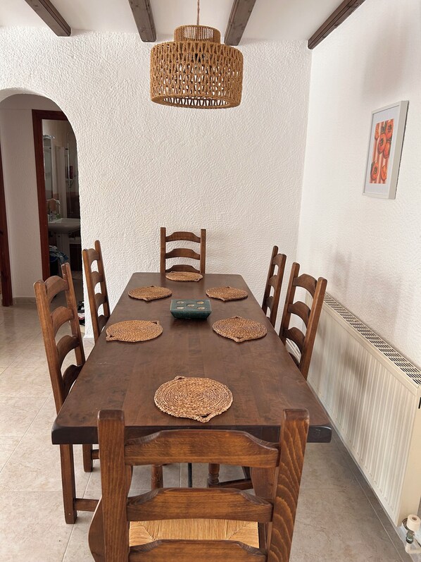 Ein Esszimmer mit Holztisch, sechs Stühlen, gewebten Tischsets und einer Hängeleuchte.