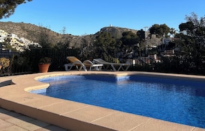 A swimming pool with lounge chairs, surrounded by a fence and trees, with buildings in the background. - El Portet, Moraira - Fully Refurbished 3-Bed With Pool, 6-Min Walk To The Beach (Moraira)