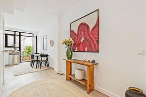 Un interior modern amb zona de menjador, una taula de consola amb un ram i un quadre abstracte gran.