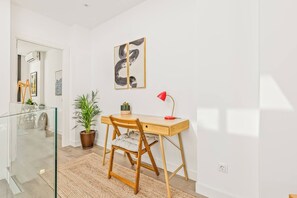 Une pièce moderne avec un bureau en bois, une lampe de bureau rouge, une plante en pot et un grand tableau abstrait accroché au mur.