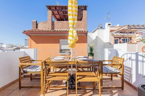 Une terrasse sur le toit, avec une table en bois dressée pour deux personnes, entourée de chaises et agrémentée d’un parasol à rayures jaunes.