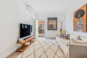 A modern living room with a flat-screen TV, a sofa, a patterned rug, and a door leading to an outdoor area. - Coral8 - Top modern townhouse in Estepona old town (Estepona)